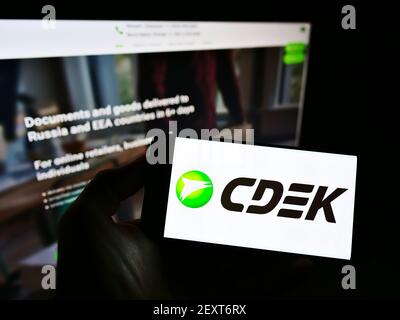 Person holding smartphone with logo of Russian logistics company CDEK on screen in front of website. Focus on phone display. Unmodified photo. Stock Photo