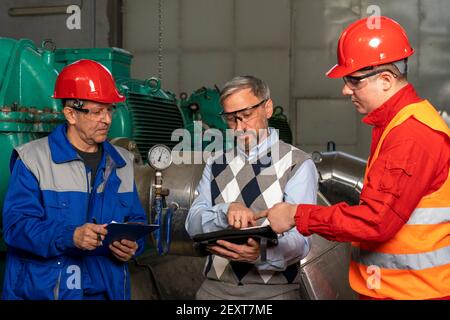 Technical Manager Using Digital Tablet and Talking to Two Power Plant Workers. District Heating Power Plant. Digital Technology Concept. Industry 4.0 Stock Photo
