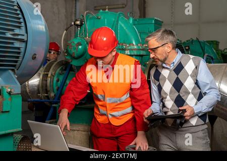 Worker Using Laptop Computer in Mechanical Room. Portrait of Young Worker in District Heating Power Plant. Digital Technology Concept. Industry 4.0 . Stock Photo