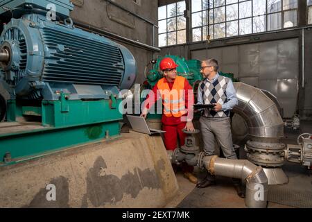 Manager with Digital Tablet Talking to Power Plant Worker with Laptop Computer. District Heating Power Plant. Digital Technology and Teamwork Concept. Stock Photo