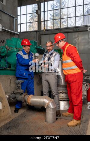 Technical Manager Using Digital Tablet and Talking to Two Power Plant Workers. District Heating Power Plant. Digital Technology and Teamwork Concept. Stock Photo
