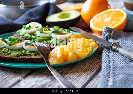 Open sandwich with avocado and boiled sliced eggs served with fresh fruits on a bamboo plate on kitchen table at home Stock Photo