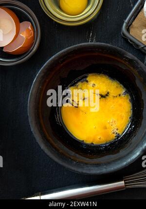 Beaten egg yolks in a bowl on a dark background. Close up Stock Photo