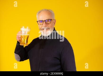 Senior handsome man drinking jar of beer standing over isolated yellow background Stock Photo