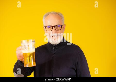 Senior handsome man drinking jar of beer standing over isolated yellow background Stock Photo