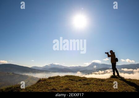 Silhouette of a backpacker photographer taking pictures of morning landscape in autumn mountains with digital camera. Stock Photo