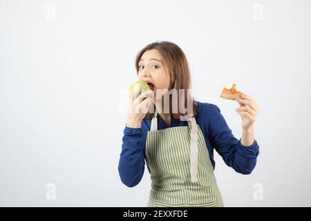 Portrait of a cute young woman in apron eating a fresh green apple Stock Photo