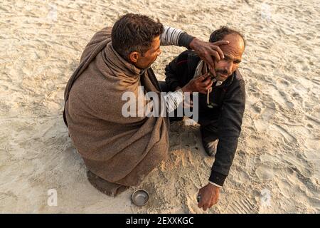 a barber cutting the hair of pilgrim during the kumbh mela in haridawar.kumbh is the largest congregation on the earth. Stock Photo