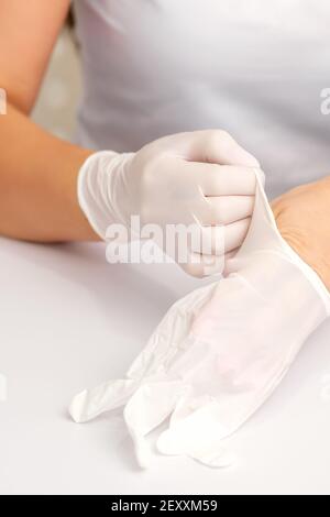 Close up of hands of nurse or female doctor puts on white rubber protective gloves over the table Stock Photo