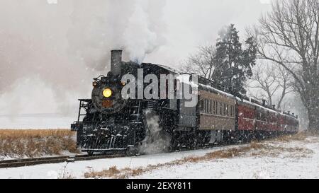 View of An Antique Restored Steam Locomotive Blowing Smoke and Steam Traveling Thru Farmlands and Countryside in a Snow Storm Stock Photo