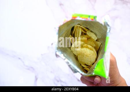 holding a packer of tasty potato chips on wooden background . Stock Photo