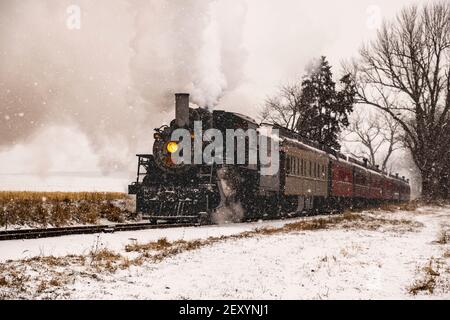 View of An Antique Restored Steam Locomotive Blowing Smoke and Steam Traveling Thru Farmlands and Countryside in a Snow Storm Stock Photo