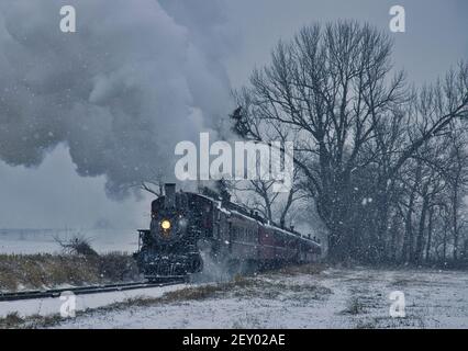 View of An Antique Restored Steam Locomotive Blowing Smoke and Steam Traveling Thru Farmlands and Countryside in a Snow Storm Stock Photo