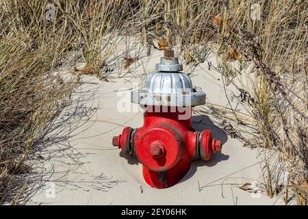 Old red fire hydrant partially buried in the sand Stock Photo