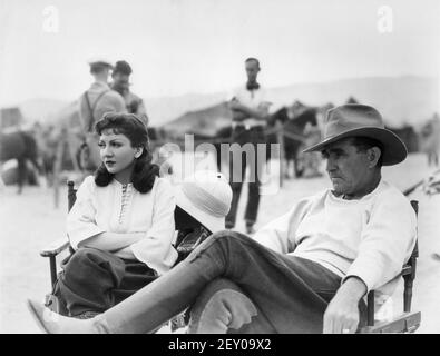 CLAUDETTE COLBERT and Director FRANK LLOYD on set location candid during filming of UNDER TWO FLAGS 1936 director FRANK LLOYD novel Ouida A Darryl F. Zanuck Production / 20th Century Pictures / Twentieth Century Fox Stock Photo