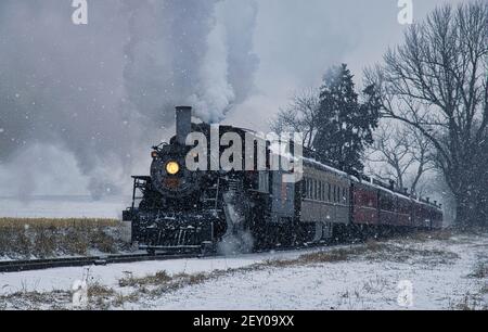 View of An Antique Restored Steam Locomotive Blowing Smoke and Steam Traveling Thru Farmlands and Countryside in a Snow Storm Stock Photo