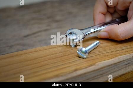 Close-up of a joiner hand with a wrench screwing nut a furniture screw into a wooden plank, The effort  wrong of tools as a fail concept Stock Photo