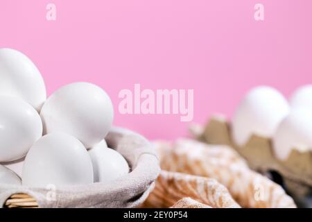 White Chicken eggs in a cardboard box and in a Straw basket on a pink background with piece of cloth, Raw Fresh Chicken Eggs in a paper container Stock Photo
