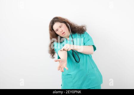 Young female doctor with down syndrome checking her pulse over white wall Stock Photo