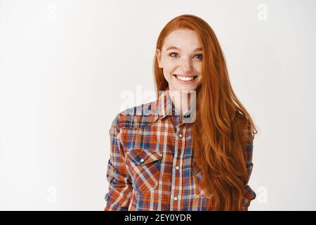 Happy young ginger girl smiling and looking surprised, standing over white background Stock Photo