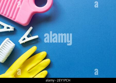 Washboard, clothespins, brush, rubber gloves on blue background. Laundry and cleaning concept. top view, copy space Stock Photo