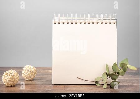 mockup of notebook with white blank sheet of paper stands on wooden table on gray background decorated with dry flowers Stock Photo