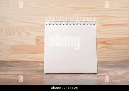 mockup image. square notebook with blank page stands upright on wood table against a wooden wall background. space for your text, message or design. B Stock Photo