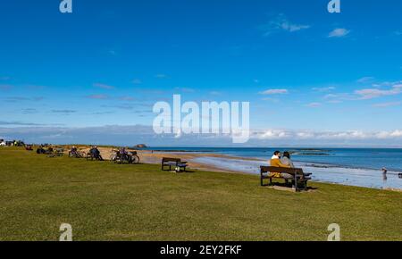 People sitting on benches on beach seafront overlooking Firth of Forth, North Berwick, East Lothian, Scotland, UK Stock Photo