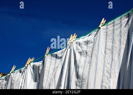 Cotton pillowcases held by wooden clothes pegs, drying on clothes line  on a sunny day. Stock Photo