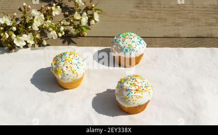 Three Easter cake on a white tablecloth with a branch of a blossoming apple tree. Spring holiday concept. Horizontal orientation. Copy space. Stock Photo