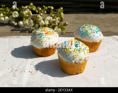 Three Easter cake on a white tablecloth with a branch of a blossoming apple tree. Spring holiday concept. Horizontal orientation. Copy space. Selectiv Stock Photo