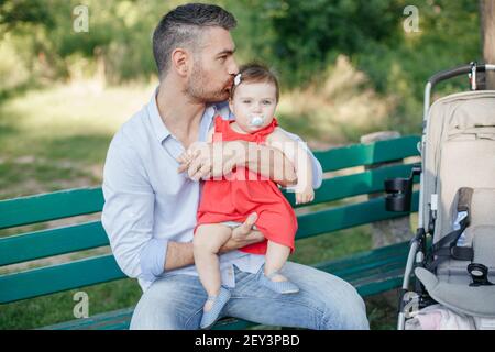 Caucasian proud father holding and kissing baby daughter. Family dad and daughter walking together outdoor in park on summer day. Life with kids child Stock Photo