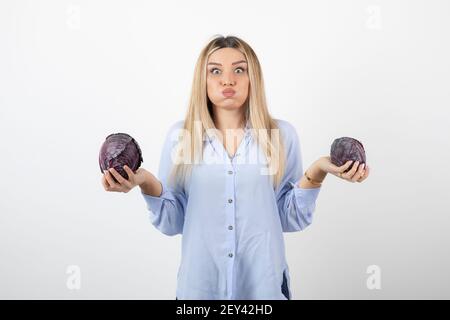 Beautiful woman in blue outfit holding purple cabbage over white wall Stock Photo