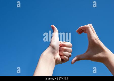 Close-up of two hands making a thumb up sign, half heart on a blue background, copy space. Friendzone concept, romantic relationship, flirting Stock Photo