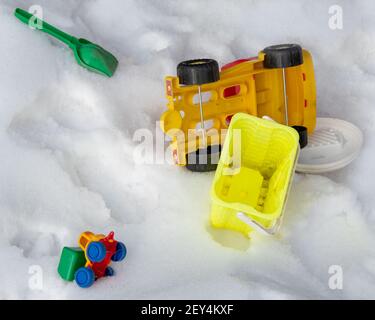 Forgotten children's toys green scoop, typewriter, yellow bucket, yellow big car in the snow. close-up. without people. Stock Photo