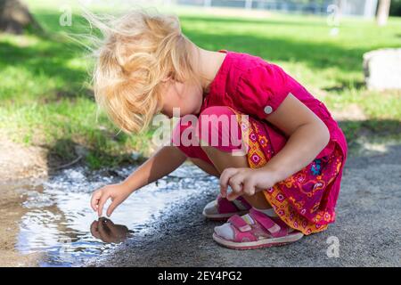 Child playing with dirty puddle barefoot in the park in summer. Happy childhood without electronic gadgets concept Stock Photo