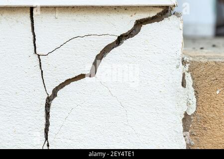 A house white wall with a large crack. Grunge concrete cement white wall with a crack in an industrial building. Stock Photo