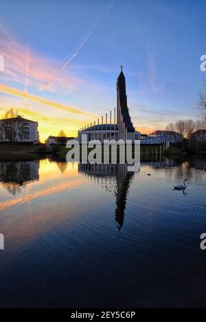 A beautiful catholic church reflecting in a lake while the sun is setting in a dramatic way Stock Photo