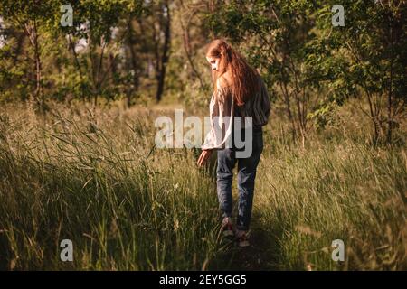 Back view of teenage girl touching grass walking on path in summer Stock Photo