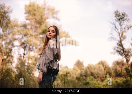 Young woman with camera standing in forest during summer Stock Photo