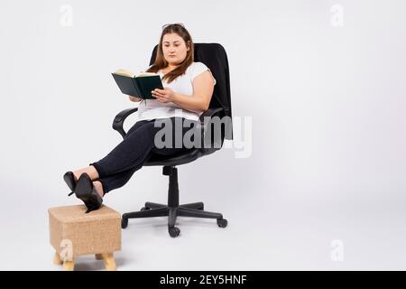 Young overweight woman accountant in glasses working in office, making notes in diary, filing taxes, providing outsource accounting service. Stock Photo