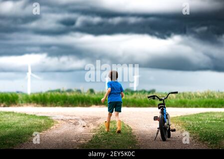 boy with bicycle watching storm clouds over a wind farm in Iowa Stock Photo