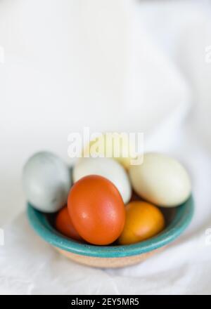 Naturally dyed yellow orange and blue Easter Eggs in a clay bowl Stock Photo