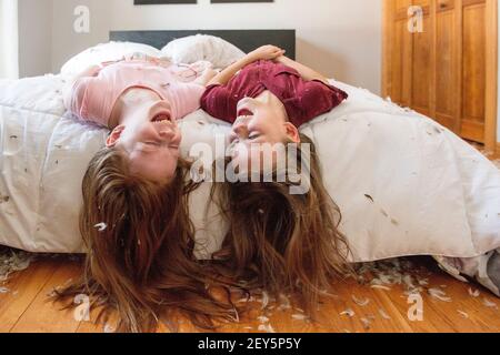 Two happy young girls having a feather pillow fight on the bed. Stock Photo