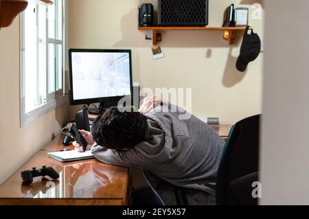 Bored man using a phone in a room full of technology during a long day Stock Photo