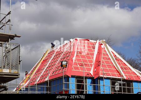 Scaffolding at a house currently under construction protected from the weather. Workmen working on the roof. Clouds in the sky. Netherlands, March Stock Photo