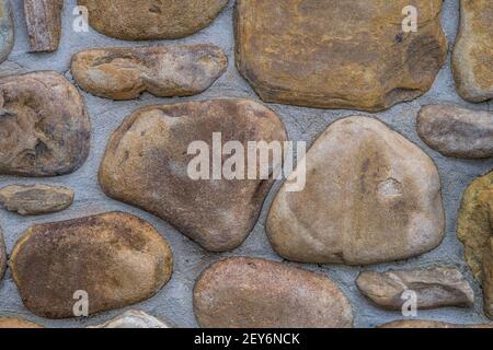 Variety of river rocks made into a stone wall on a building closeup surrounded by mortar exterior Stock Photo