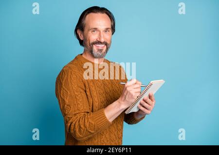 Photo portrait of smiling positive journalist writing article in notepad with pen isolated on bright blue color background Stock Photo