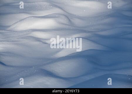 close up of mounds fo snow after fresh snow fall in winter cold temperatures sun shining on fresh snow crystals shadows behind bumps of snow in field Stock Photo
