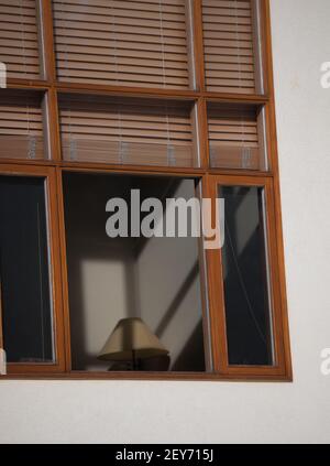 brown window blinds or shades blocking light coming through exterior wood framed home window light casting shadows on onterior wall sof home and lamp Stock Photo